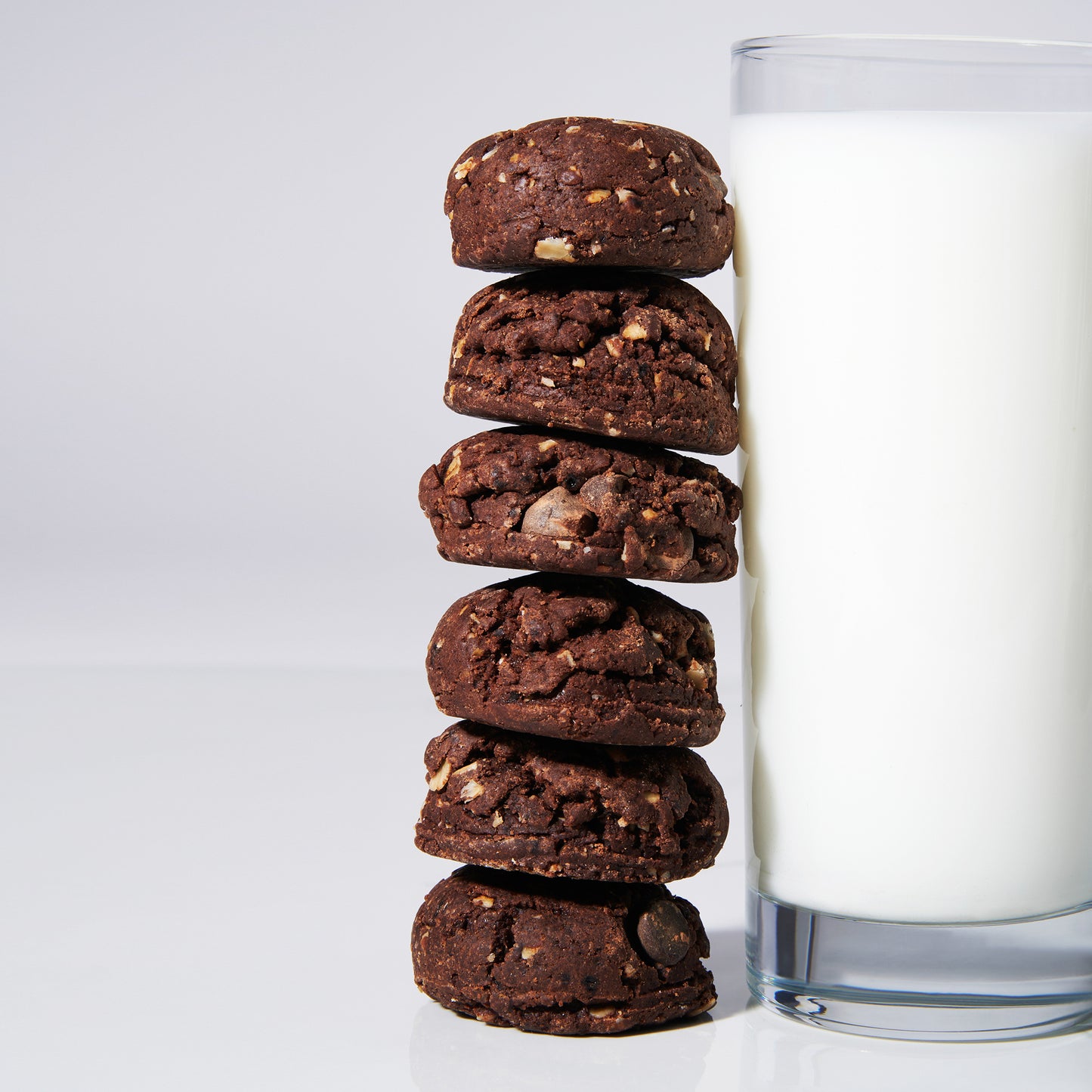 Six Mocha Oat Chocolate Chip Cookies on a white background leaning against a glass of non-dairy milk