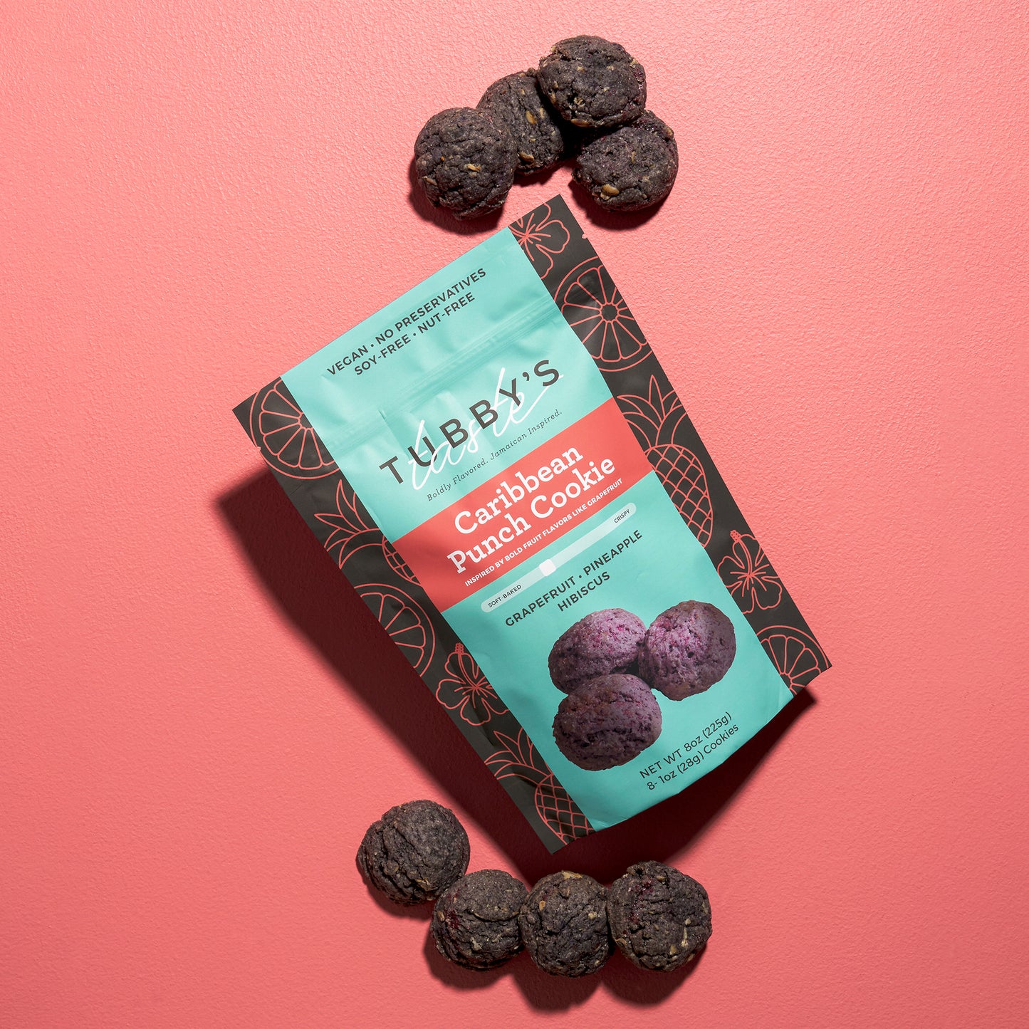 Eight Purple Grapefruit Pineapple Hibiscus cookies labeled Caribbean Punch come out of a bag of Tubby's Taste on a pink background.